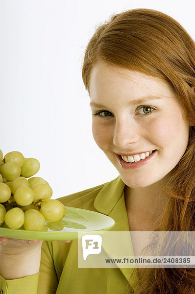 Portrait of a young woman holding a plate of grapes and smiling