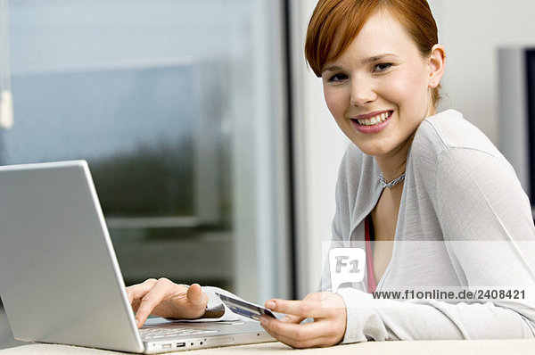 Portrait of a young woman holding a credit card and using a laptop