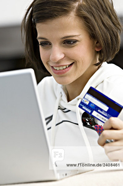 Close-up of a young woman holding a credit card and using a laptop