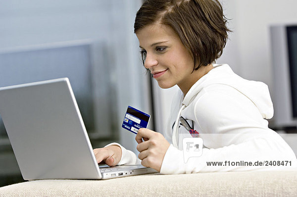 Side profile of a young woman holding a credit card and using a laptop