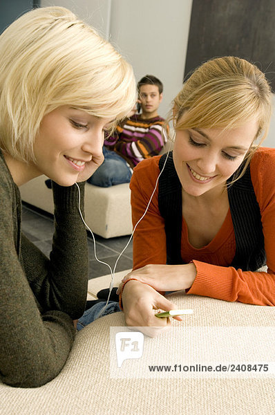 Zwei junge Frauen  die einen MP3-Player hören und lächeln.