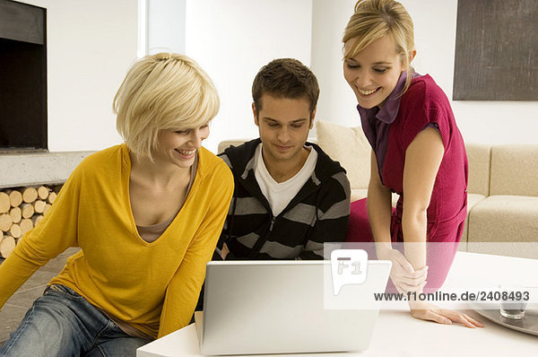 Junger Mann mit zwei jungen Frauen beim Blick auf einen Laptop