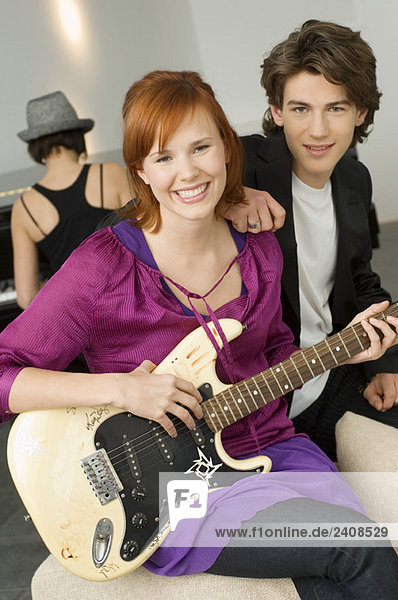 Porträt einer jungen Frau  die Gitarre spielt  mit einem Jungen  der neben ihr sitzt.