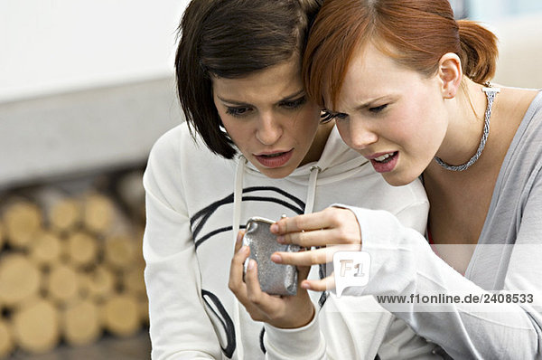 Zwei junge Frauen  die in eine Wechselgeldbörse schauen.