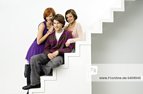 Porträt eines Teenagers  der mit zwei jungen Frauen auf einer Treppe sitzt und lächelt.