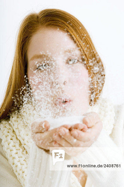 Nahaufnahme einer jungen Frau  die Schnee aus ihren hohlen Händen bläst.