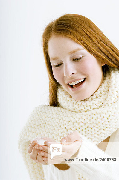 Close-up of a young woman holding snow in cupped hands and smiling