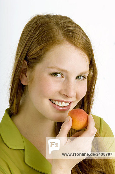 Porträt einer jungen Frau  die eine Aprikose isst und lächelt