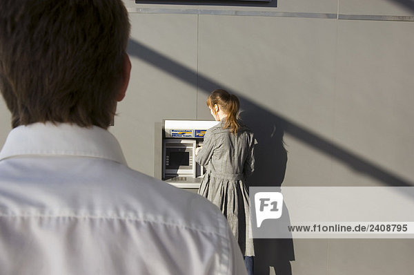 Rückansicht eines Geschäftsmannes Blick auf eine Geschäftsfrau mit einem Geldautomaten