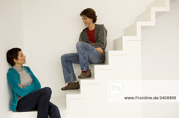 Mittlere erwachsene Frau und ihr Sohn sitzen auf einer Treppe.