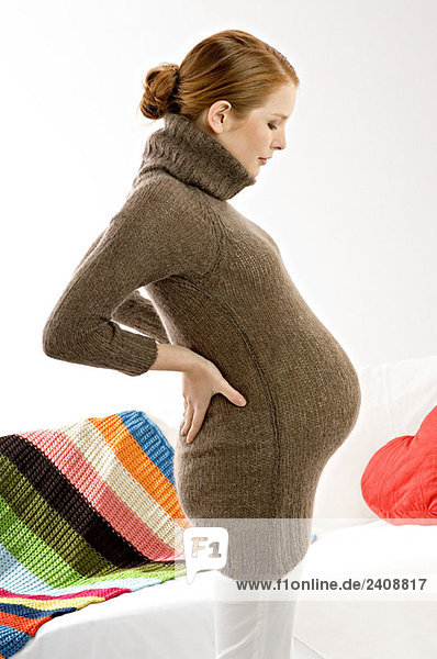 Side profile of a pregnant young woman standing and looking at her abdomen