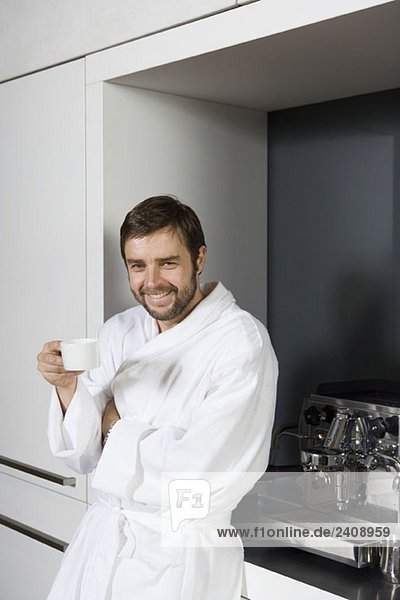 Ein lächelnder Mann im Bademantel mit einer Kaffeetasse.