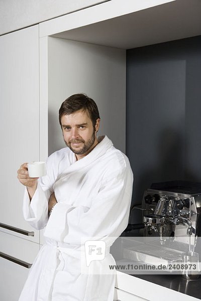 Ein Mann im Bademantel hält eine Kaffeetasse.