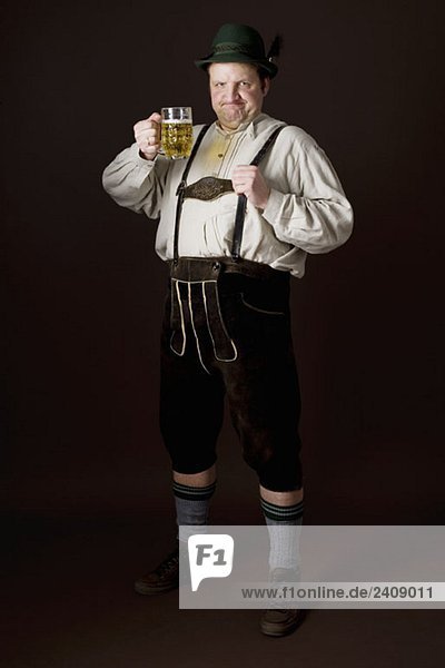 Stereotypischer deutscher Mann in bayerischer Tracht  der ein Bier in Toast zubereitet.
