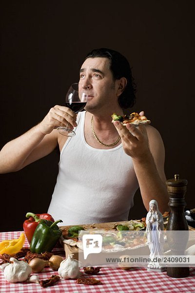 Stereotypischer Italiener hält ein Weinglas und isst Pizza.