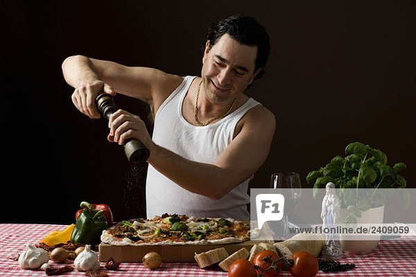 Stereotypischer Italiener  der eine Pfeffermühle auf seiner Pizza benutzt.