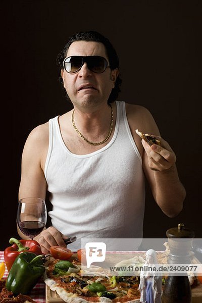 Stereotypischer Italiener  der Pizza isst und ein Messer hält.