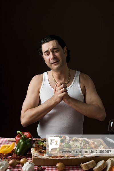 Stereotypischer Italiener mit in Dankbarkeit umklammerten Händen beim Anblick einer Pizza