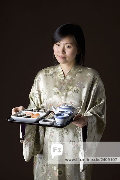 Eine Frau in einem Kimono  die ein Tablett mit Sushi und Tee trägt.