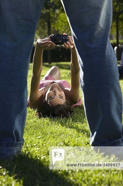 Eine junge Frau  die auf Gras liegt und einen Mann fotografiert.