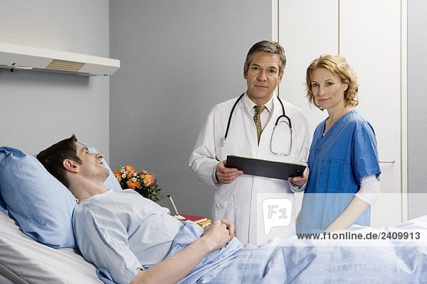 Zwei Mitarbeiter des Gesundheitswesens stehen neben einem Patienten im Bett.