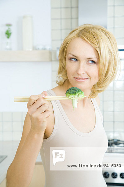 Blonde Frau hält Stück Brokkoli mit Stäbchen