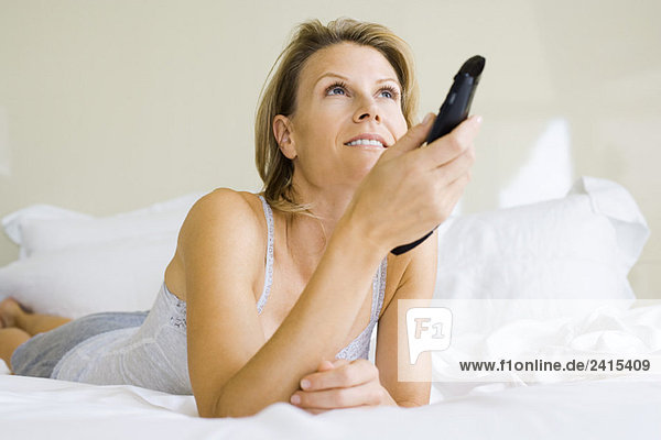 Frau auf dem Bett liegend  Kanalwechsel mit Fernbedienung