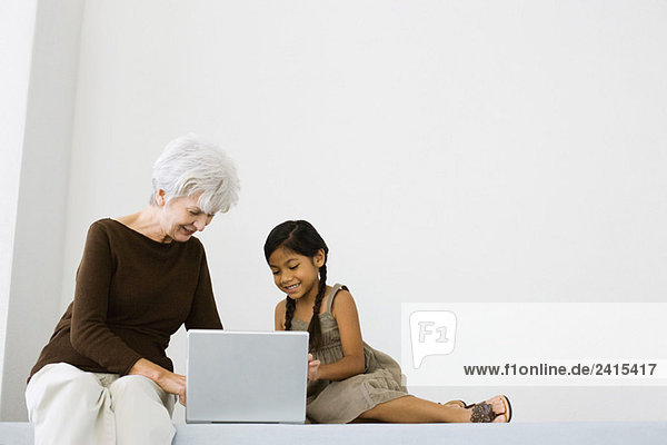 Senior woman using laptop with little girl