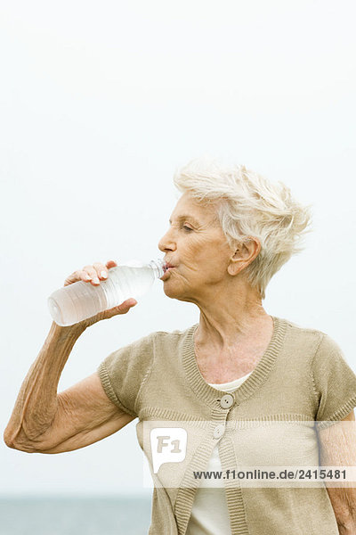Seniorenfrau trinkt Flasche kaltes Wasser