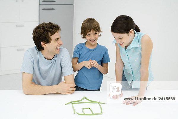 Vater und zwei Kinder mit grünen Bohnen in Form eines Hauses  alle lächelnd.