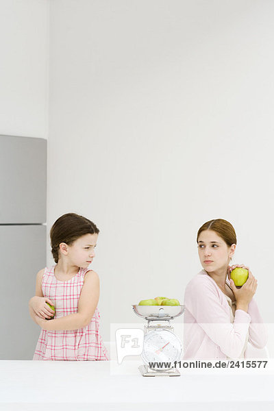 Mutter und Tochter wiegen Äpfel auf einer Waage  jeder hält Apfel und runzelt die Stirn.
