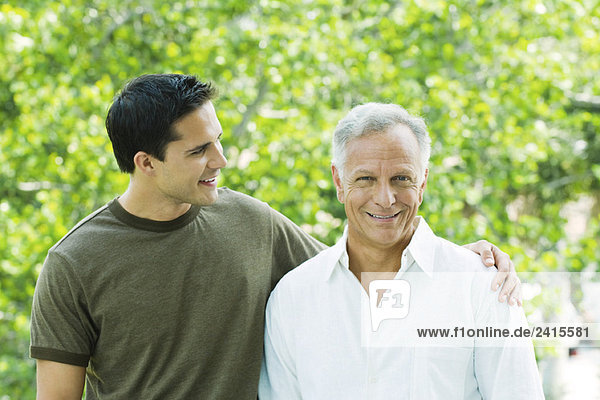 Young man with arm around father's shoulder  father smiling at camera