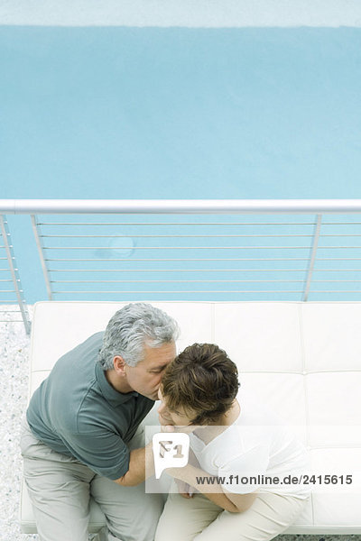 Paar auf dem Balkon sitzend,  Mann küsst die Wange der Frau,  hoher Blickwinkel