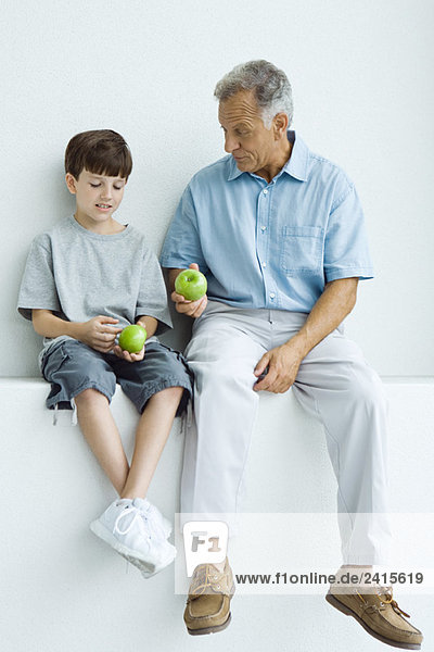 Grandfather and grandson sitting together on ledge  both holding apples