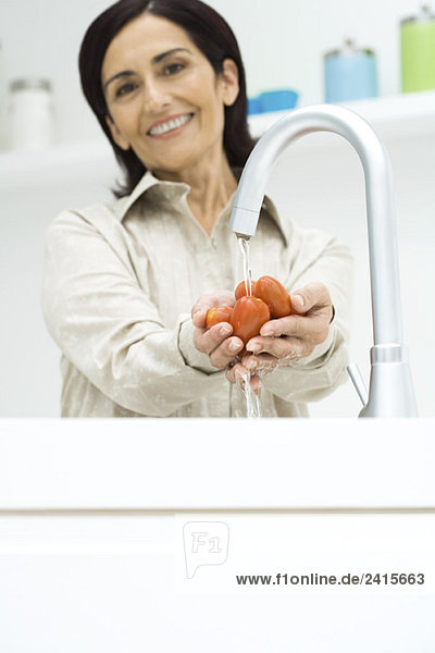 Frau spült Roma-Tomaten unter Wasserhahn  lächelt in die Kamera