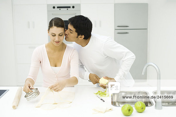 Ein Paar kocht zusammen  ein Mann küsst die Wange einer Frau.
