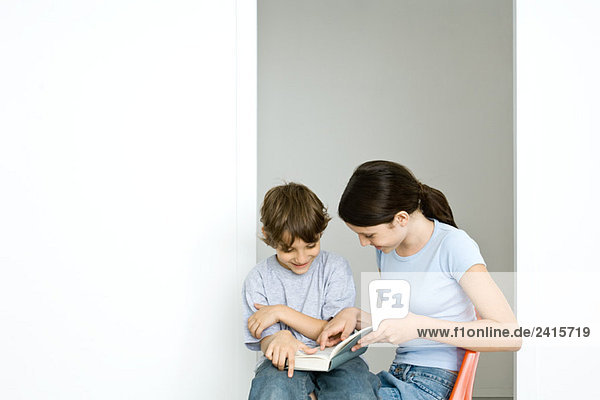 Preteen Mädchen und kleiner Bruder lesen Buch zusammen