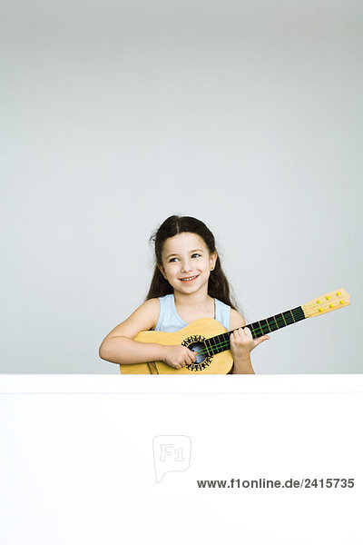 Kleines Mädchen spielt Spielzeuggitarre  lächelt