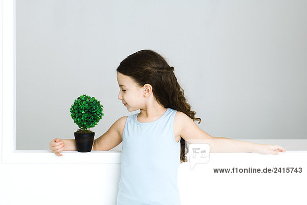 Kleines Mädchen mit Arm um Topfpflanze stehend