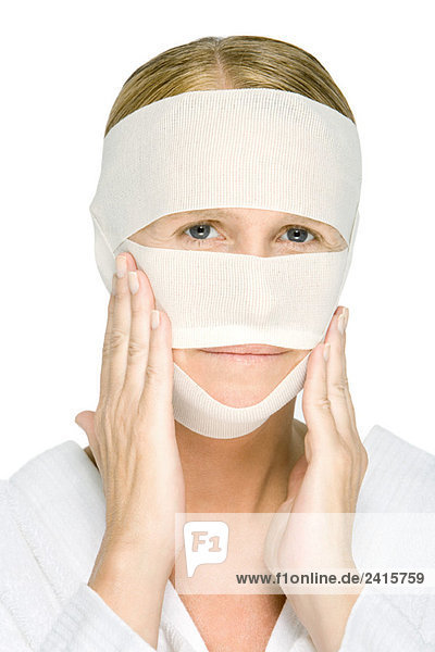Frau mit bandagiertem Gesicht  berührende Wangen  Blick in die Kamera