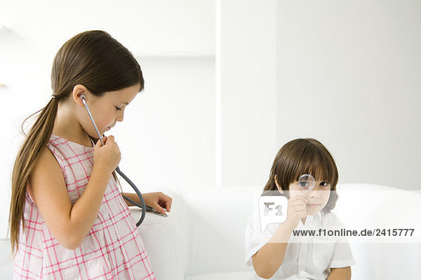 Kleiner Junge schaut durch Lupe auf die Kamera  Mädchen hört Stethoskop