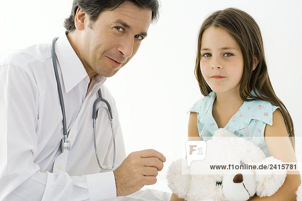 Doktor mit kleinem Mädchen sitzend  beide lächelnd vor der Kamera