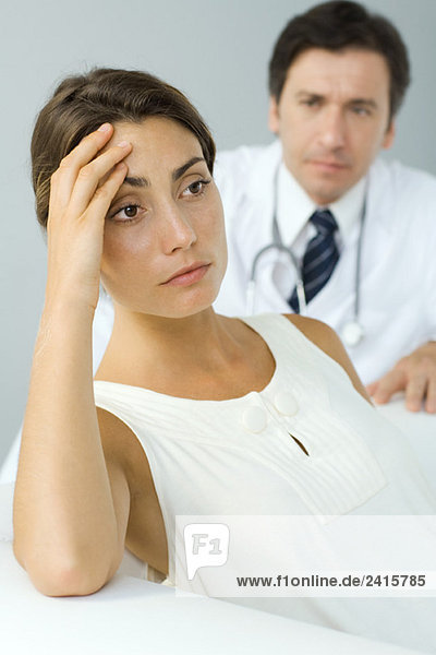 Frau hält Kopf  schaut weg  Arzt im Hintergrund