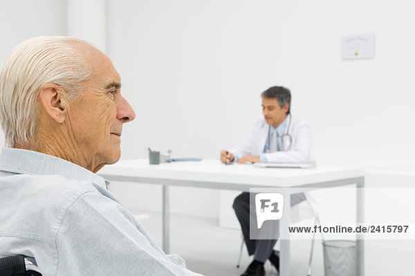 Doctor working at desk  focus on senior patient in foreground