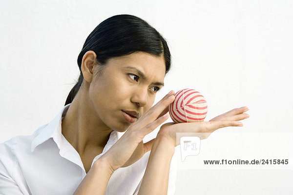 Woman holding striped ball in open palm  looking away