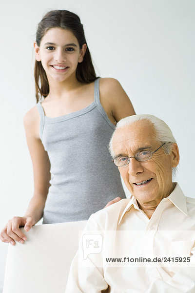 Preteen girl standing behind grandfather  both smiling at camera