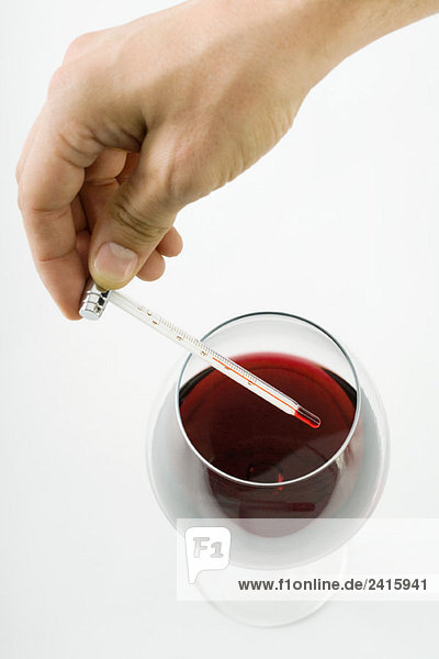 Person hält Thermometer über Glas Rotwein  abgeschnittene Handansicht