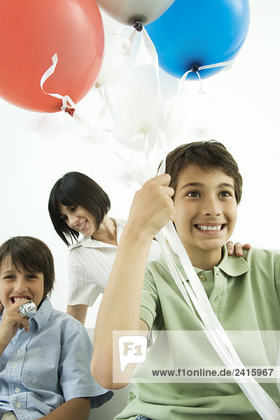 Junge mit Heliumballons  lächelnd  Mutter und Bruder im Hintergrund