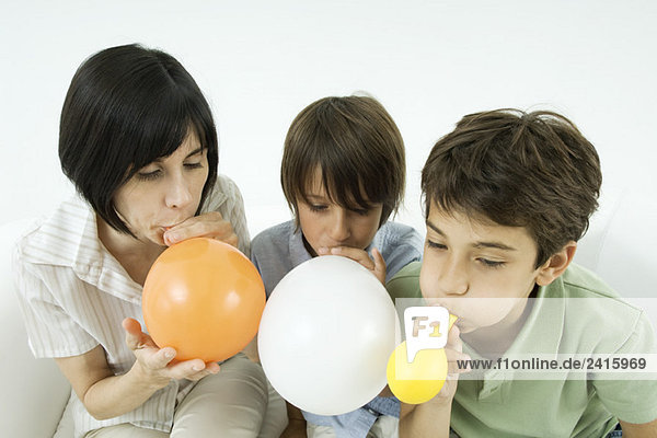 Mutter und zwei Söhne beim Aufblasen von Luftballons