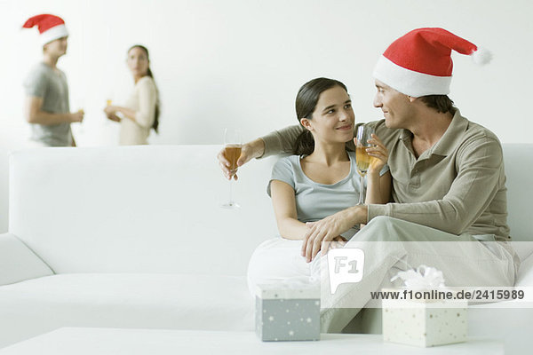 Paar auf dem Sofa sitzend  Champagner trinkend  Mann mit Weihnachtsmütze